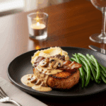 Plated bacon mushroom pork chop with mashed potatoes and green beans.