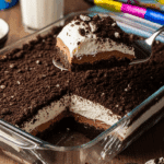 Glass dish of Oreo Delight being served with a spatula, next to a glass of milk.