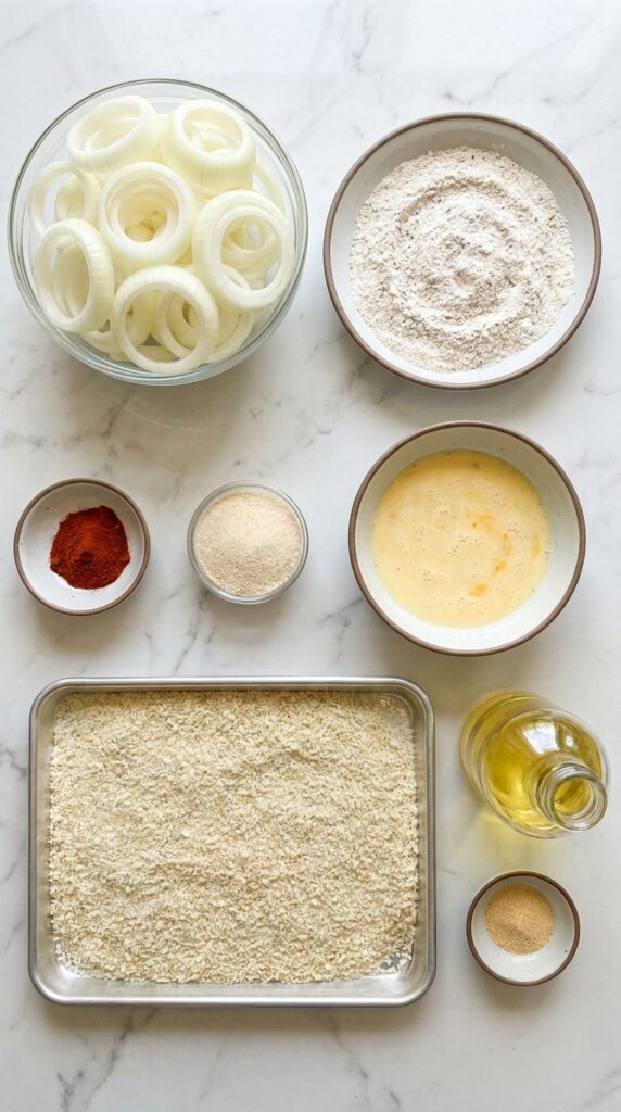 A flat lay showing the three-step dredging station for onion rings with onions, flour, buttermilk, and Panko.