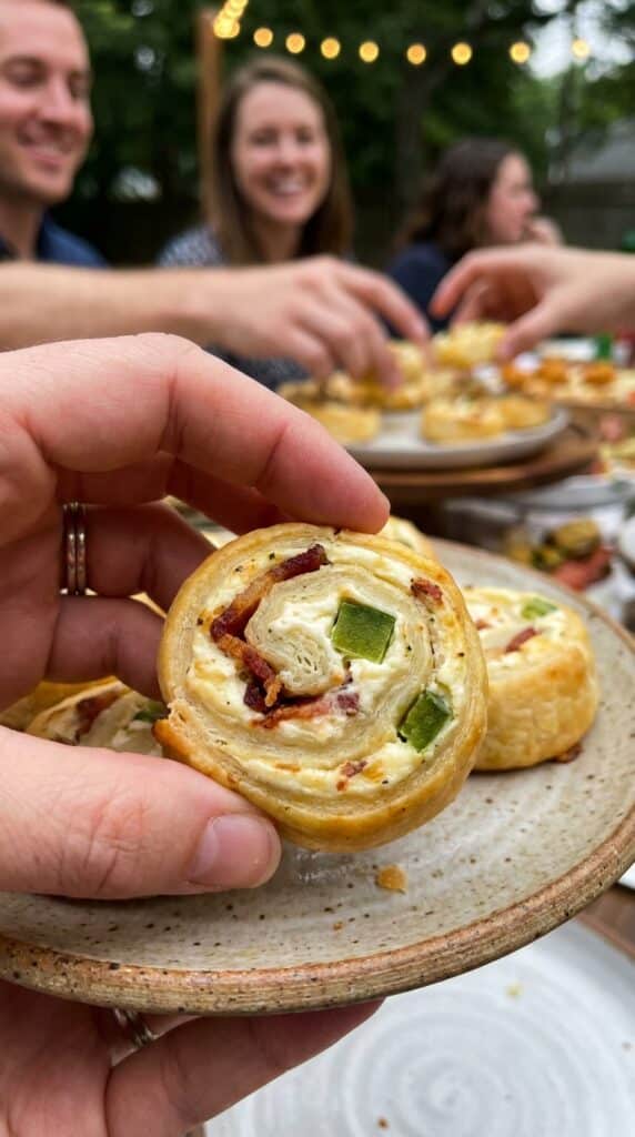 A close-up of a hand holding a jalapeno popper pinwheel, showing the creamy filling and diced jalapenos.
