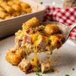A close-up of a serving spoon lifting a scoop of Chicken Bacon Ranch Tater Tot Casserole onto a plate.