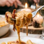 A fork lifting a creamy piece of rigatoni pasta and chicken, with the sauce dripping and steam rising.