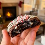 A hand holds a broken Peppermint Oreo cookie, showing the soft, fudgy interior with Oreo chunks inside.