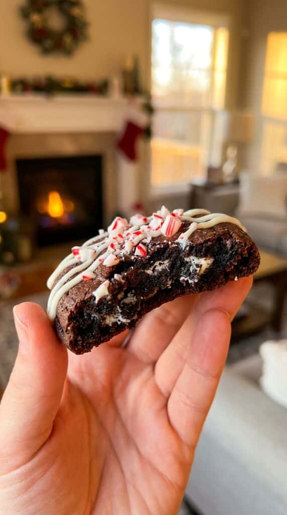 A hand holds a broken Peppermint Oreo cookie, showing the soft, fudgy interior with Oreo chunks inside.
