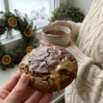 A hand holding a soft gingerbread cookie with maple glaze dripping down the side, set in a cozy winter atmosphere.