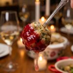 A close-up of a juicy turkey meatball on a cocktail pick, dipped in bright red cranberry sauce.