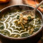 A close-up of a spoon breaking through a sour cream spiderweb on green chicken stew, lifting a hearty bite of beans and meat.