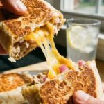 A close-up of hands pulling apart a toasted tuna wrap, revealing a gooey melted cheddar cheese pull.