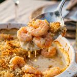 A close-up of a serving spoon lifting creamy garlic shrimp and a crispy golden breadcrumb topping out of a baking dish.
