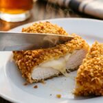 A close-up of a knife slicing into a juicy piece of parmesan crusted chicken, showing the melted cheese and crispy breadcrumb layers.