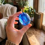 A playful, lifestyle-oriented shot showing the candy being held up to light. The interaction with the light source is essential here to show the transparency of the candy, making it look like a magical artifact.