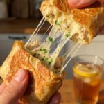 A close-up of hands pulling apart a toasted chicken wrap, creating a massive, stringy stretch of melted mozzarella cheese.