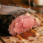 A close-up of a knife slicing a prime rib roast, revealing a perfectly pink, juicy medium-rare center and a dark herb crust.
