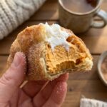 close-up of a hand holding a pumpkin pie taco with a bite taken out, showing the crispy cinnamon shell and fluffy pumpkin filling.