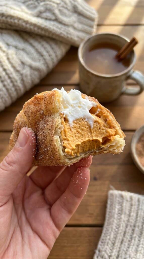 close-up of a hand holding a pumpkin pie taco with a bite taken out, showing the crispy cinnamon shell and fluffy pumpkin filling.