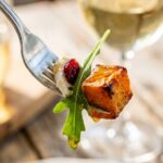A close-up of a fork holding a bite of roasted sweet potato, arugula, dried cranberry, and goat cheese coated in dressing.