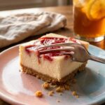 A close-up of a fork cutting through a creamy strawberry cheesecake bar, showing the dense filling and crumbly crust.