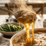 A close-up of a serving spoon lifting a scoop of hot, creamy chicken and rice casserole with steam rising.