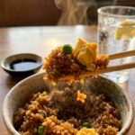 A close-up of wooden chopsticks lifting a bite of hot fried rice from a ceramic bowl.