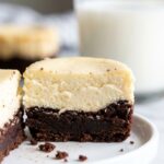 A close-up cross-section of a halved mini cheesecake showing a dense brownie bottom and a smooth cheesecake top on a white plate.