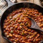 A close-up of a messy, overstuffed Cajun chicken sloppy joe sandwich on a brioche bun with the filling spilling out onto a plate.