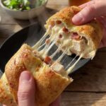 A close-up of hands pulling apart a hot chicken bake, showing a dramatic and gooey mozzarella cheese pull.