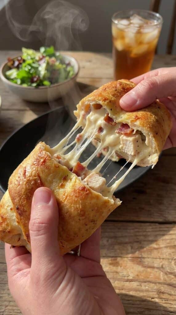 A close-up of hands pulling apart a hot chicken bake, showing a dramatic and gooey mozzarella cheese pull.