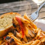 A close-up of a fork lifting a bite of creamy Cajun chicken and penne pasta from a bowl, showing a thick sauce.