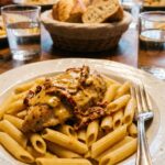 A close-up of tender chicken and creamy sun-dried tomato sauce served over penne pasta on a white plate