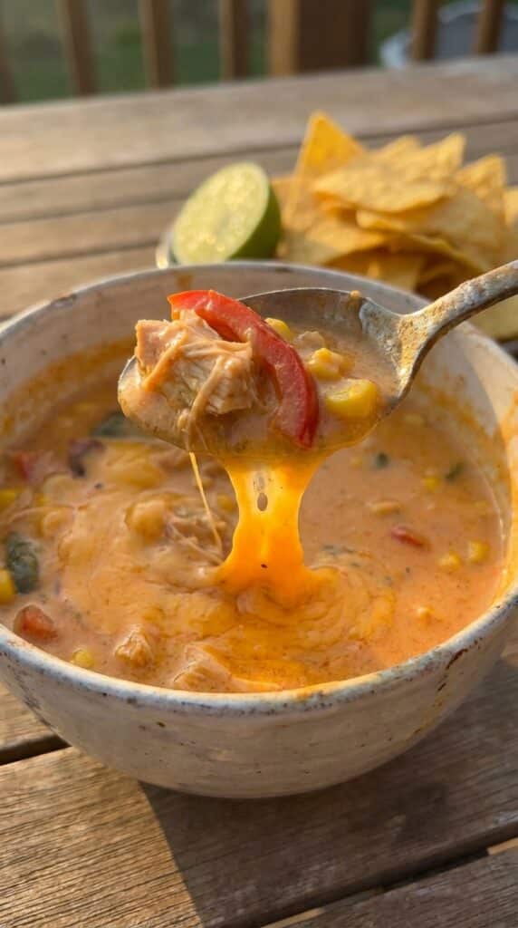 A close-up of a spoon lifting creamy chicken fajita soup with a dramatic melted cheese pull stretching back to the bowl.