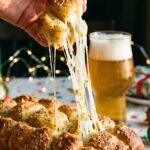 A close-up of a hand pulling a piece of garlic monkey bread away from the ring, creating a long, gooey cheese stretch.