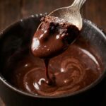 A macro close-up of a spoon holding a bite of baked chocolate cake dripping with hot molten chocolate fudge.