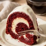 A close-up of a slice of red velvet bundt cake showing a thick white cheesecake ring baked into the center, with a fork taking a bite.