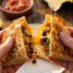 Hands pulling apart a hot, crispy pocket taco with a long string of melted cheese stretching between the halves.