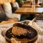 A close-up of a spoon scooping through chocolate ganache into fluffy peanut butter mousse in a glass.