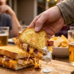A close-up of a hand grabbing a cheesy, messy slice of chicken bacon ranch bread from a party platter.