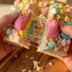 A close-up of a graham cracker scooping up melted chocolate and stringy, gooey pastel marshmallow from a skillet.