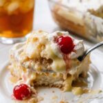 A close-up of a spoon lifting a messy, creamy bite of layered angel food cake and cherry dessert from a white plate.