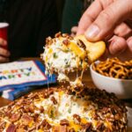 A close-up of a cracker scooping into a jalapeño popper cheese ball, revealing the creamy interior mixed with peppers and cheese.