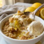 A close-up of a spoon lifting a warm, gooey bite of lemon dump cake next to melting vanilla ice cream.