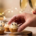 A close-up of a hand holding a single bite-sized mini cannoli cup with festive lights in the background.