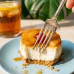A close-up of a fork cutting into a mini pineapple upside-down cheesecake, showing the creamy filling and juicy topping.