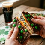 A close-up of hands breaking a piece of St. Patrick's Day chocolate toffee bark in half.