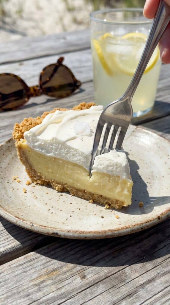 A close-up of a fork cutting into a slice of Atlantic Beach pie, showing the crumbly saltine crust, dense lemon filling, and whipped cream.