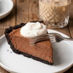 A close-up side view of a slice of Baileys chocolate pie showing the thick chocolate mousse filling, Oreo crust, and whipped cream.