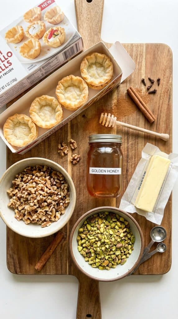 A flat lay showing boxes of mini phyllo shells, chopped nuts, honey, and cinnamon on a wooden board.