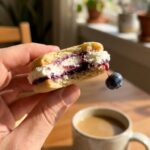 A hand holding a bitten crispy lace cookie topped with cream and fruit, showing the sharp texture.