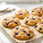 Hands tearing apart a fluffy blueberry cloud bread, revealing the airy inside and juicy berries.