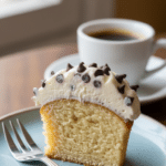 A close-up cross-section of a halved cannoli cupcake showing the moist cake and thick chocolate chip ricotta frosting.