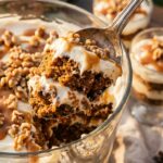 A close-up of a spoon lifting a scoop of carrot cake trifle with caramel and cream.